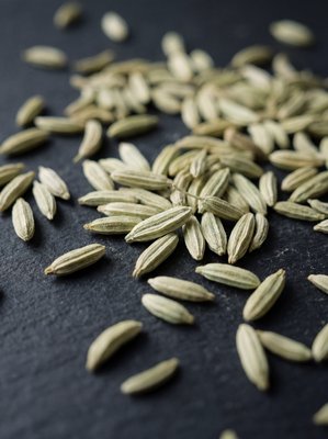 [400×400px | 72dpi | JPG] Macro food photography: Lucknow fennel seeds close-up, pale sage green elongated seeds with faint ribbing and fine texture, arranged loosely on dark matte slate, soft dramatic lighting, editorial macro style, no text